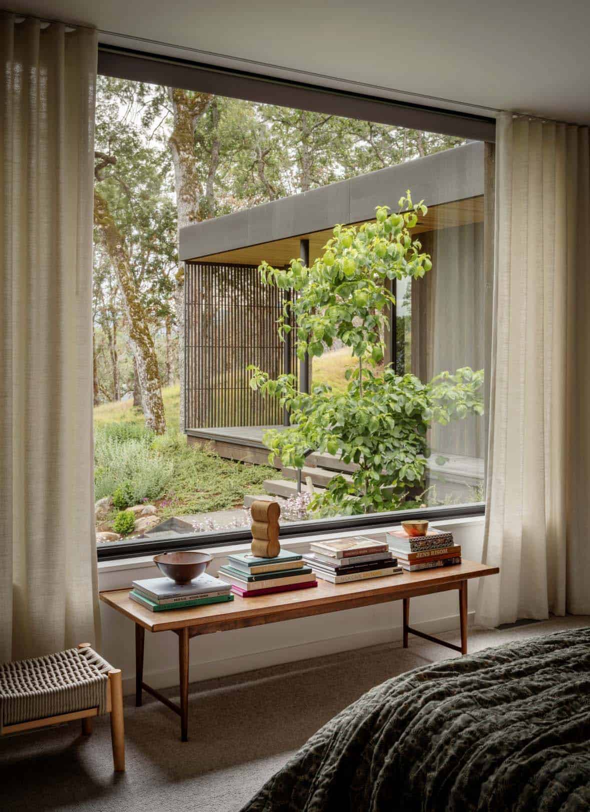 Primary bedroom window with a wood bench, linen curtains, and garden views