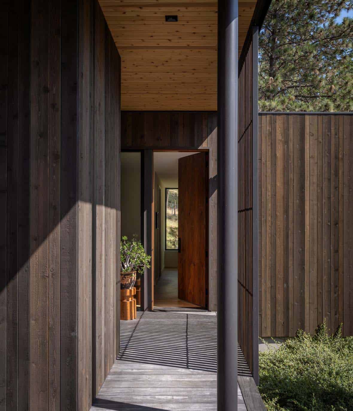 Covered entry walkway with dark cedar siding and a wood pivot door