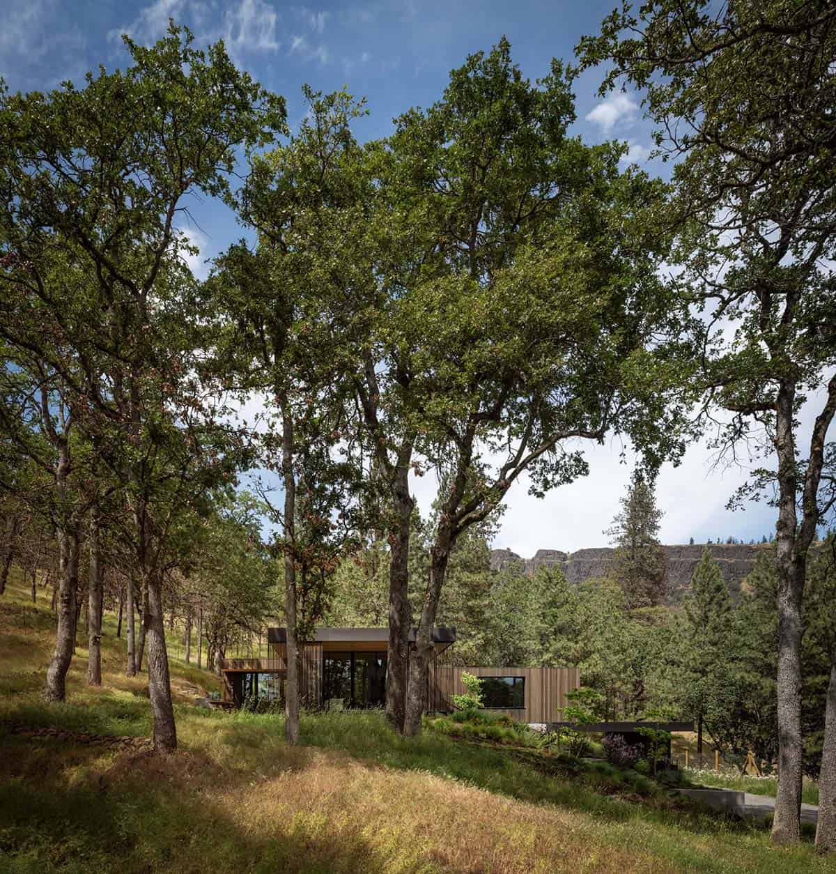 Home tucked into a sloping oak forest with a rocky cliff in the background
