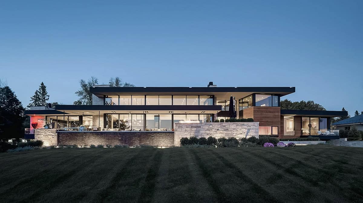 Twilight rear facade with illuminated glass walls and stone terrace