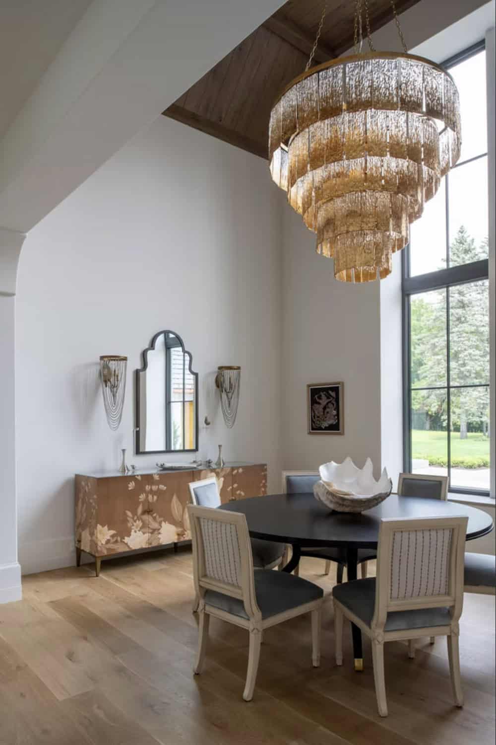 Round dining table beneath tiered gold chandelier and floral sideboard