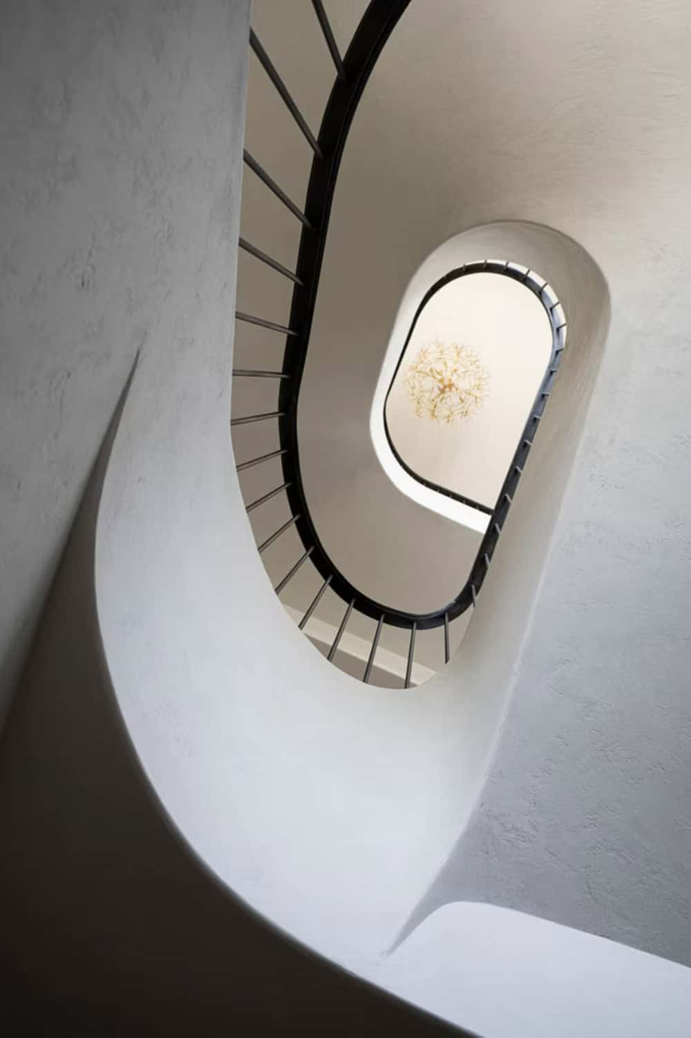 Looking down curved stairwell toward chandelier and iron railing
