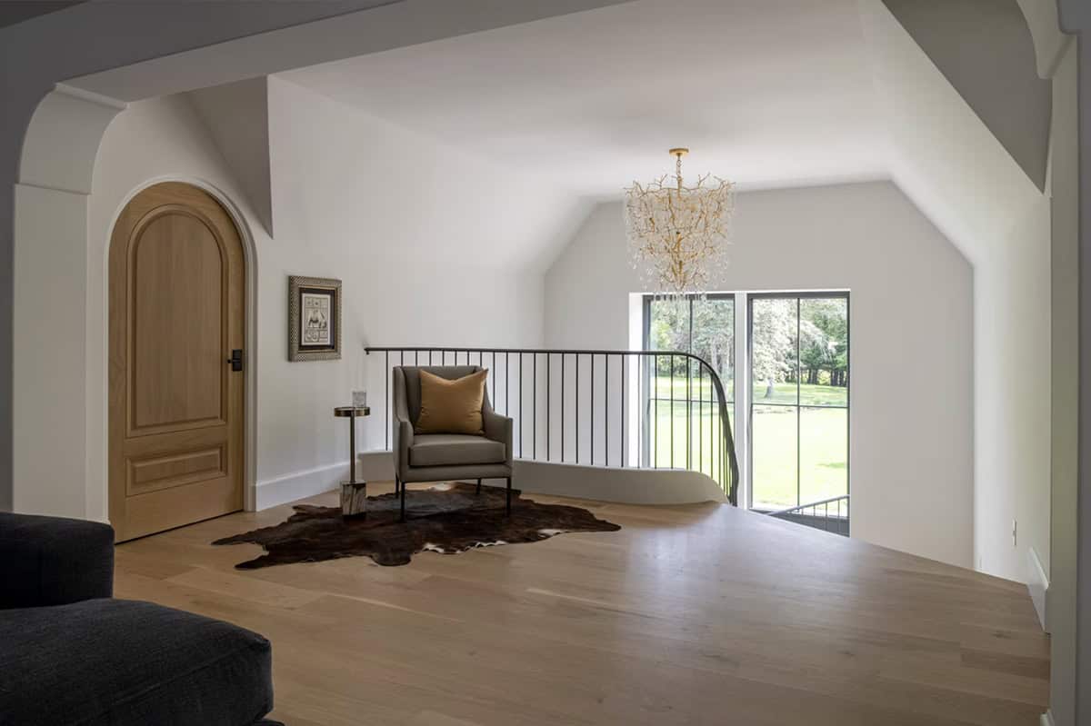 Upstairs landing with curved railing, arched door, and gold chandelier