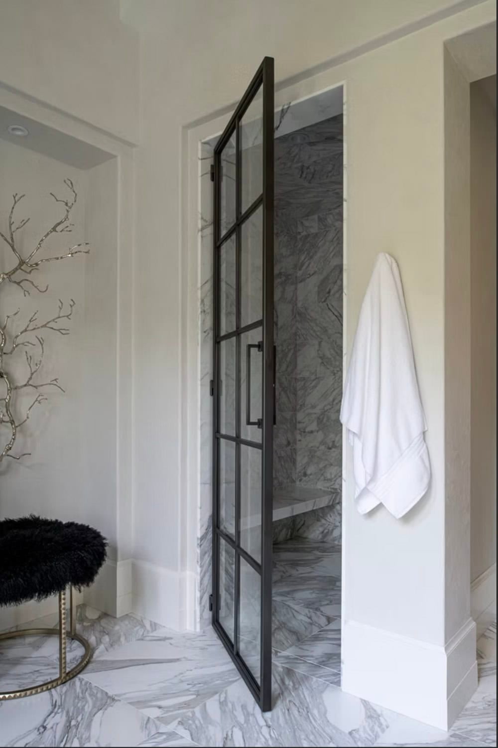 Black framed glass door opening into marble walk-in shower