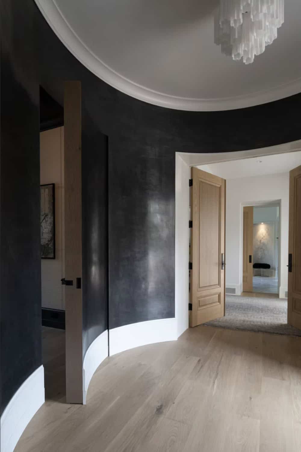 Curved black lacquered hallway with oak door and chandelier glimpse
