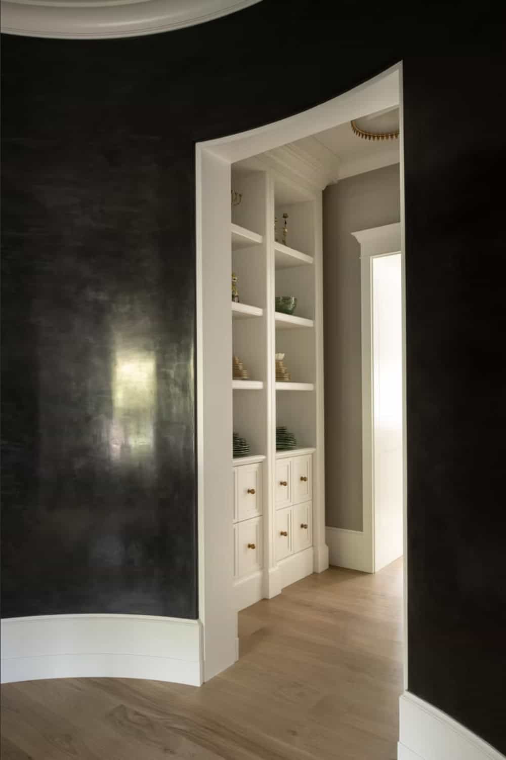 Curved black hallway opening into built-in shelving nook