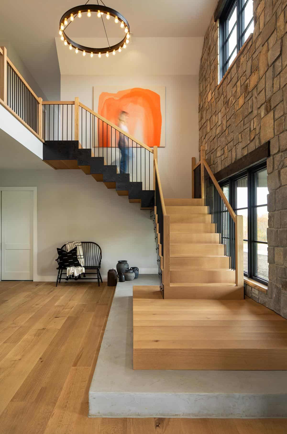 Open staircase and entry with ring chandelier and stone wall