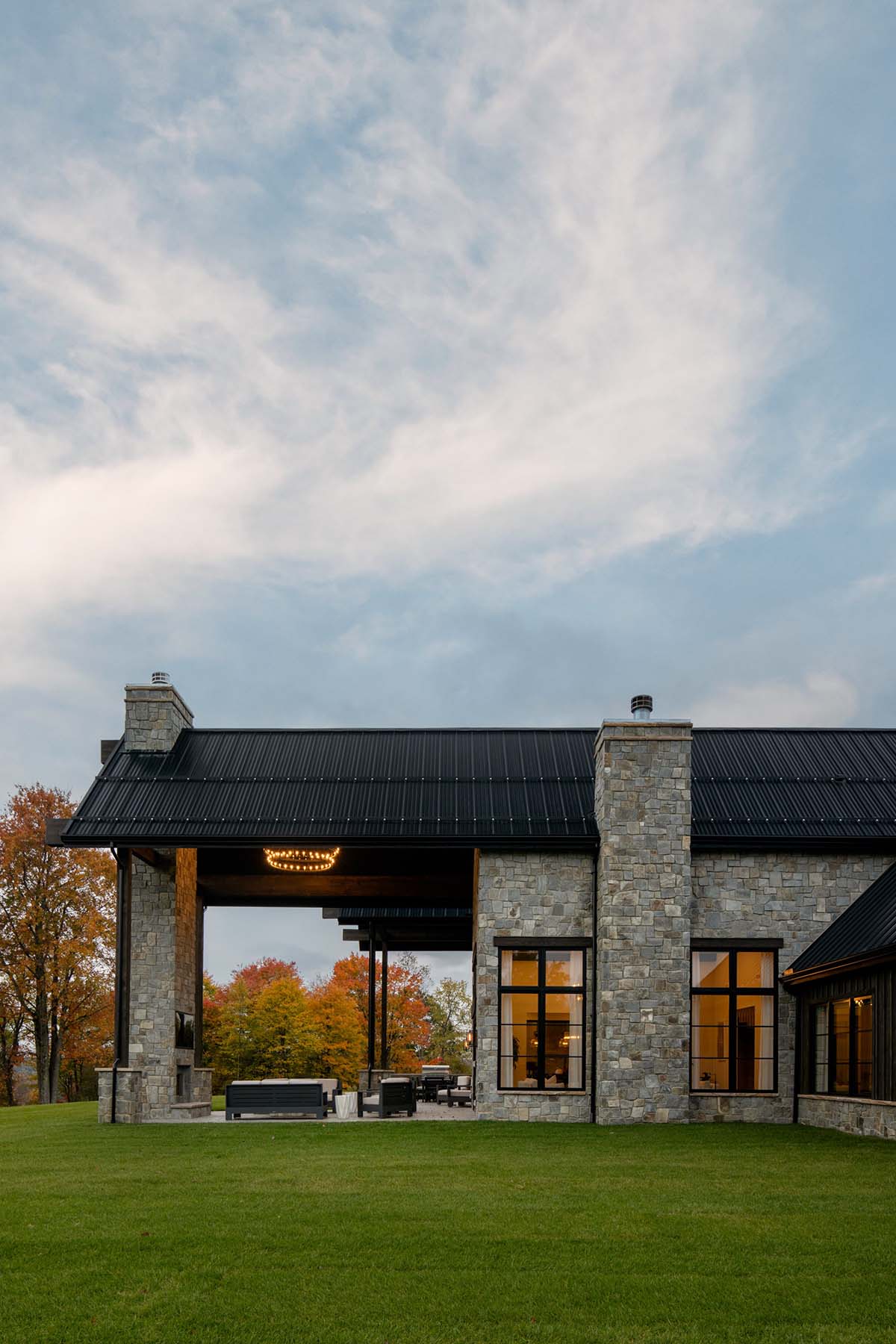 Covered patio exterior with stone chimneys and autumn tree backdrop