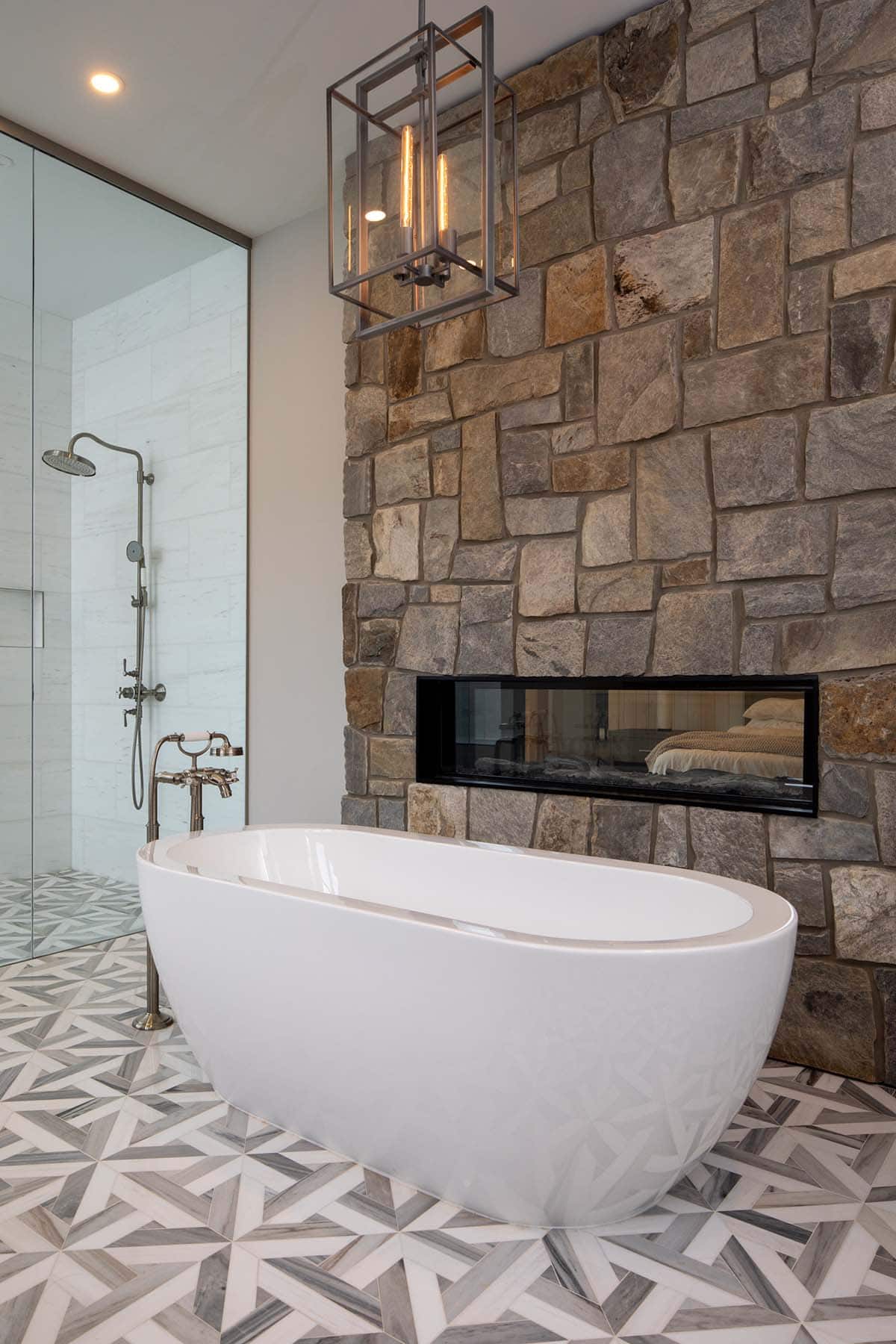 Freestanding tub beneath a stone wall with a double-sided fireplace