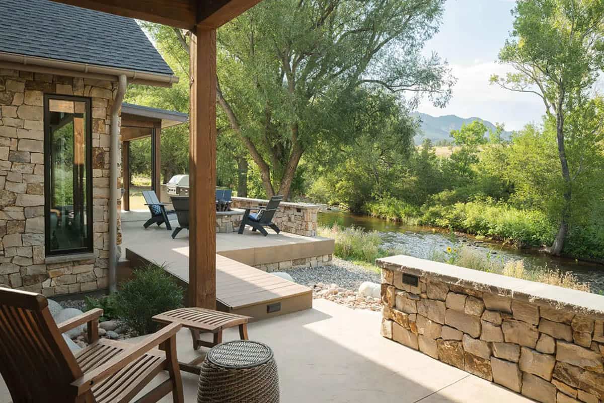Covered patio with wood chairs, low stone walls, and creek views