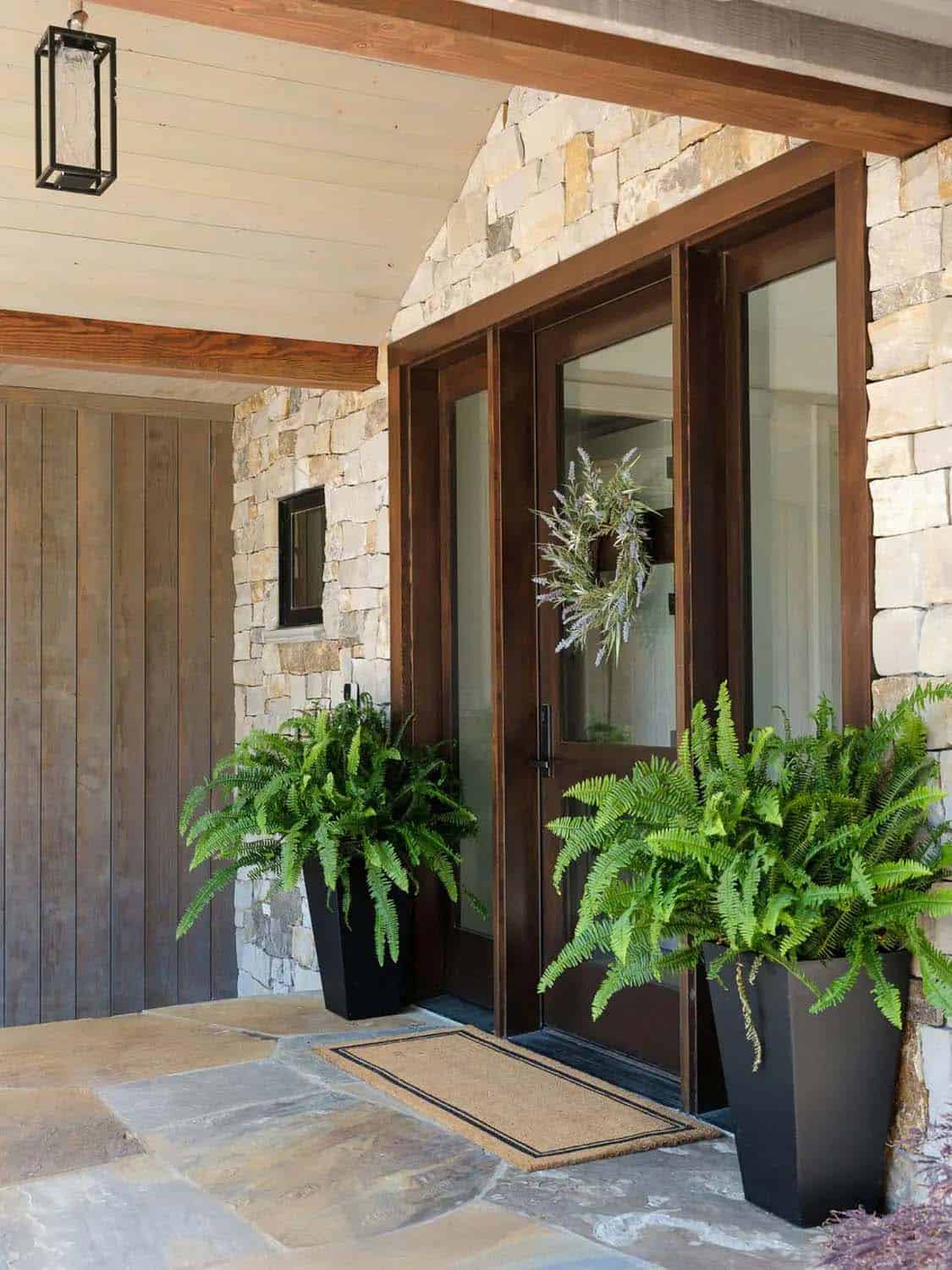 Wood front door with sidelights, wreath, and potted ferns on flagstone porch