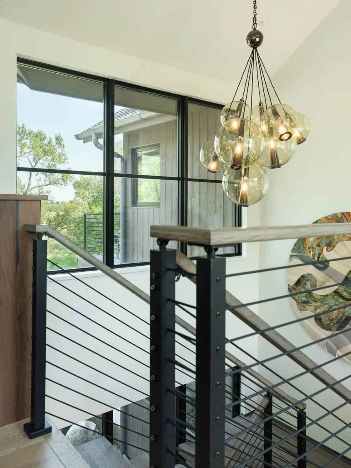 Staircase landing with black railing, glass globe chandelier, and large window