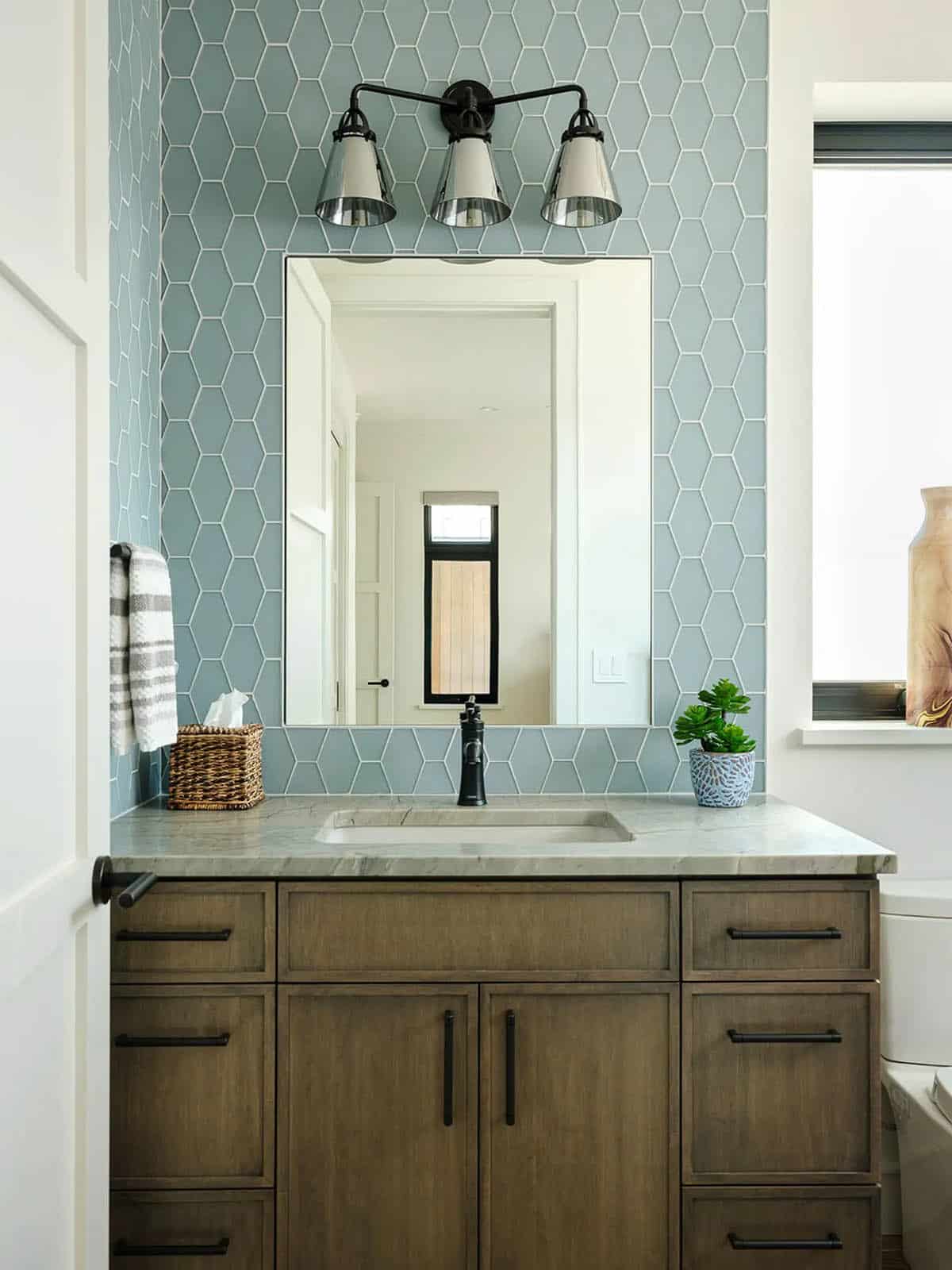 Bathroom with blue hexagon tile wall, wood vanity, and black vanity light