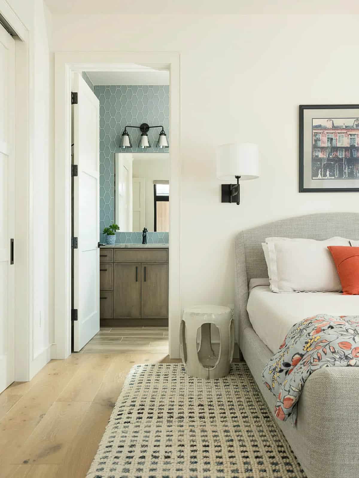 Bedroom with gray upholstered bed, ceramic stool, and blue-tiled bathroom beyond