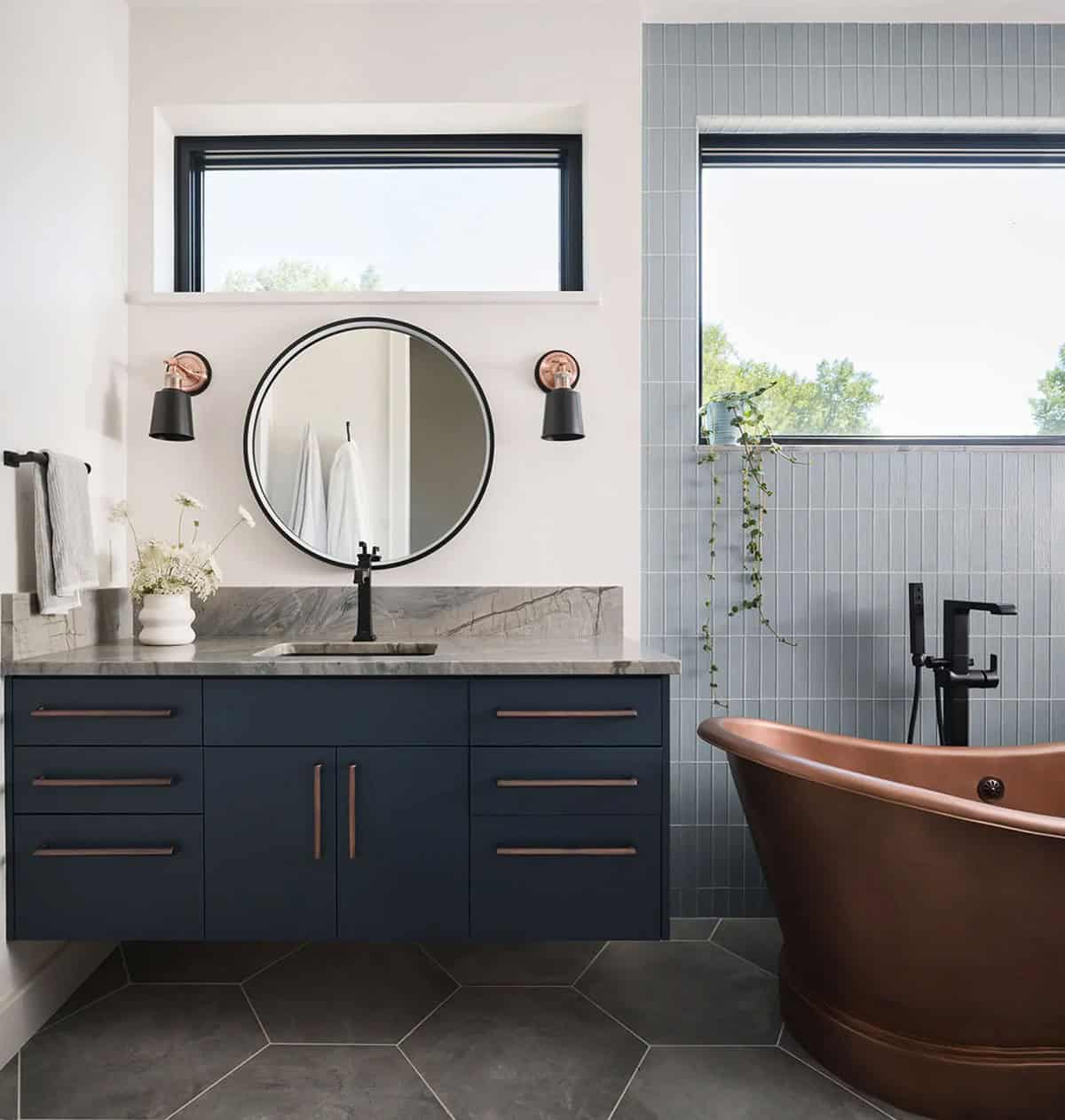 Bathroom with navy floating vanity, round mirror, and copper freestanding tub