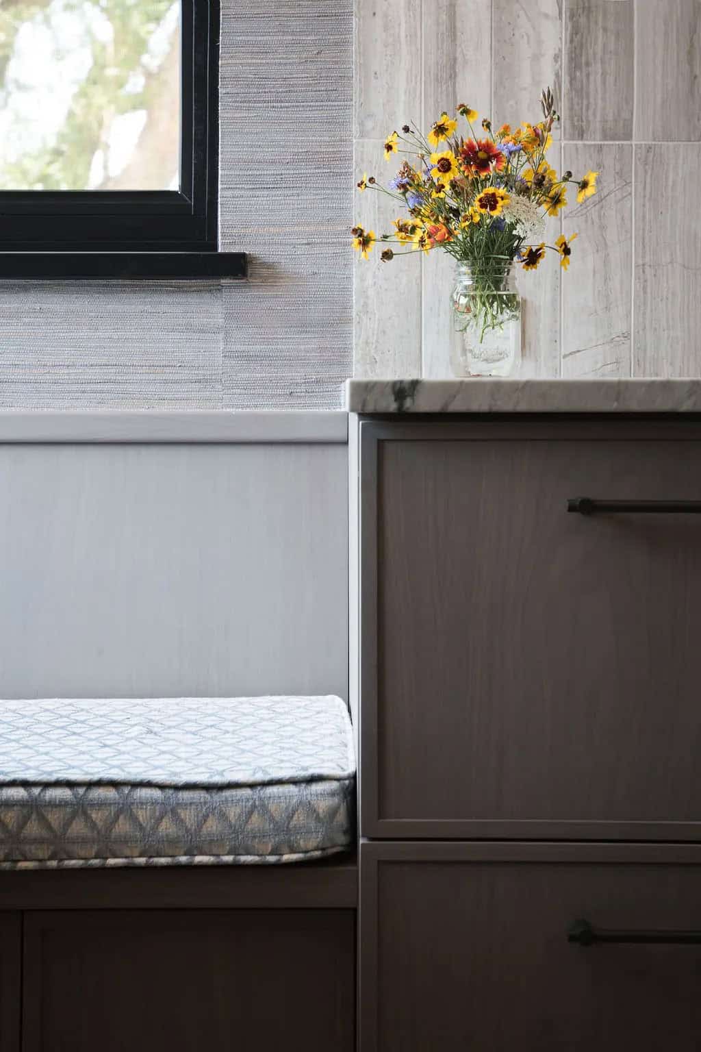 Breakfast nook bench cushion beside cabinetry with wildflowers in a mason jar