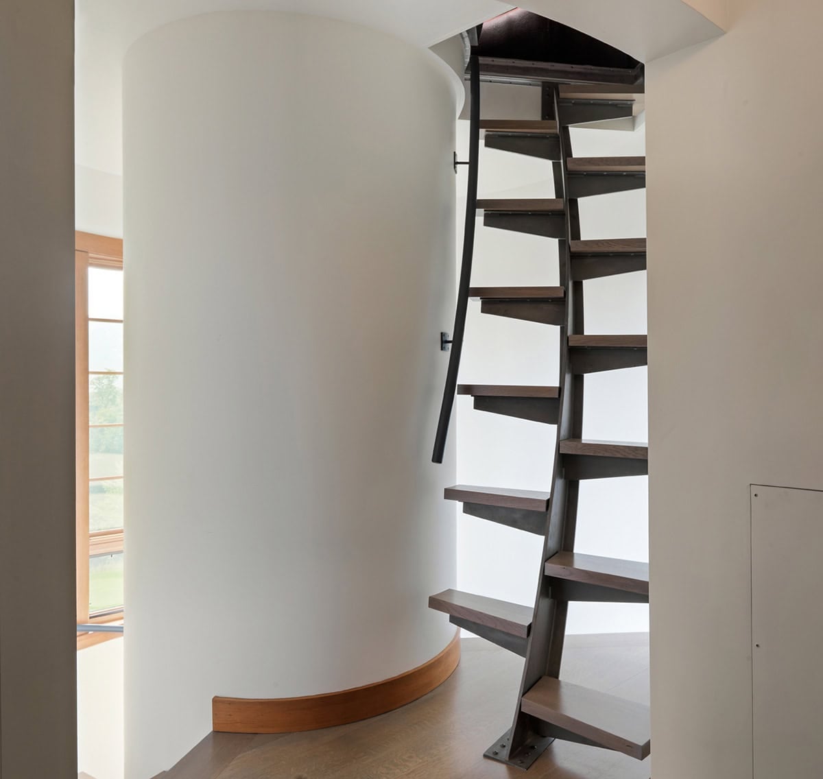 Spiral staircase with dark wood treads in curved white stairwell