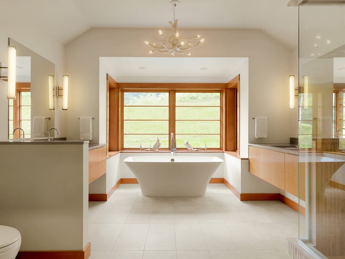 Freestanding soaking tub beneath antler chandelier with garden view window