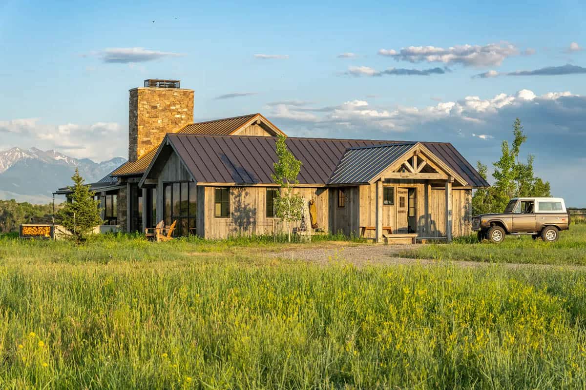 Rustic Montana home with stone chimney and vintage SUV in meadow