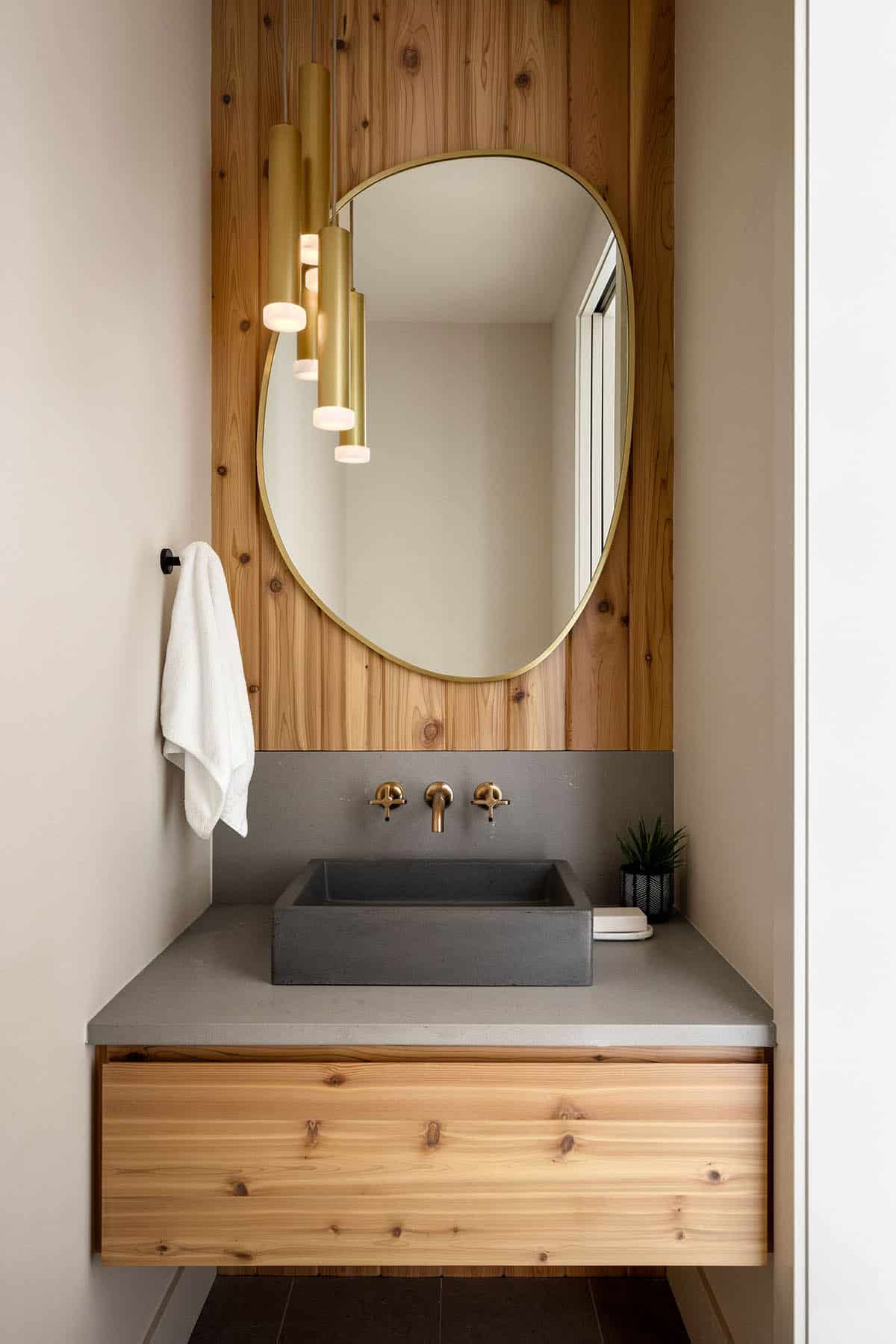 Powder room vanity with concrete sink and oval brass mirror