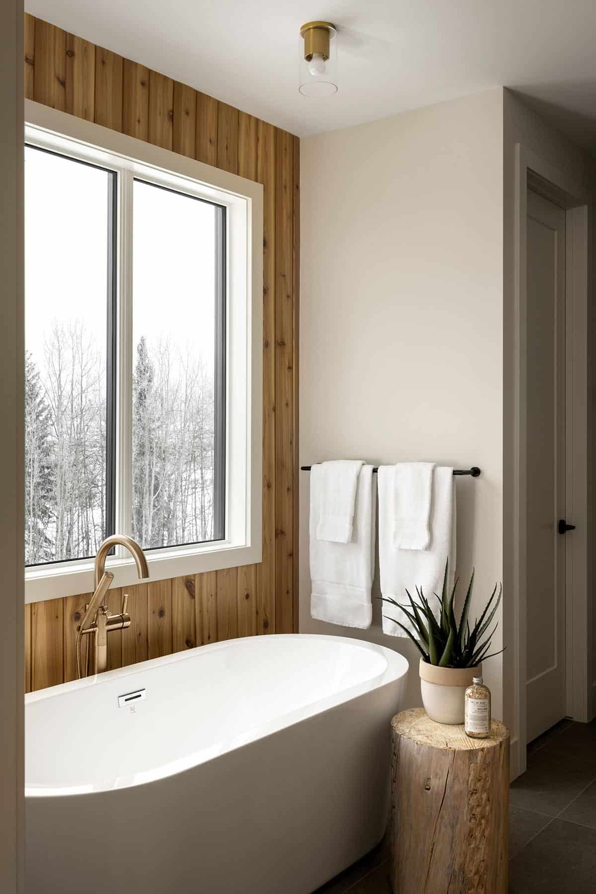 Freestanding tub beneath cedar accent wall and forest view window