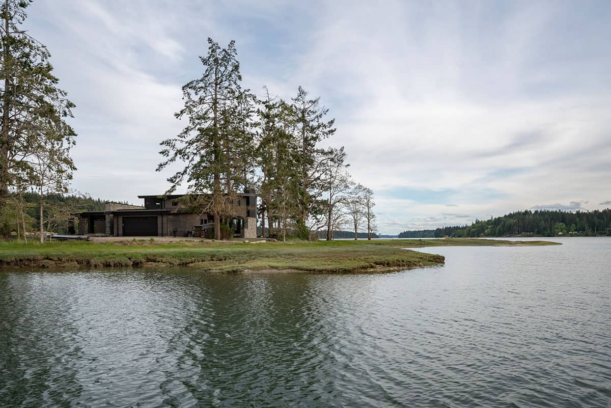 Dark-clad modern home sits at the water's edge among pines