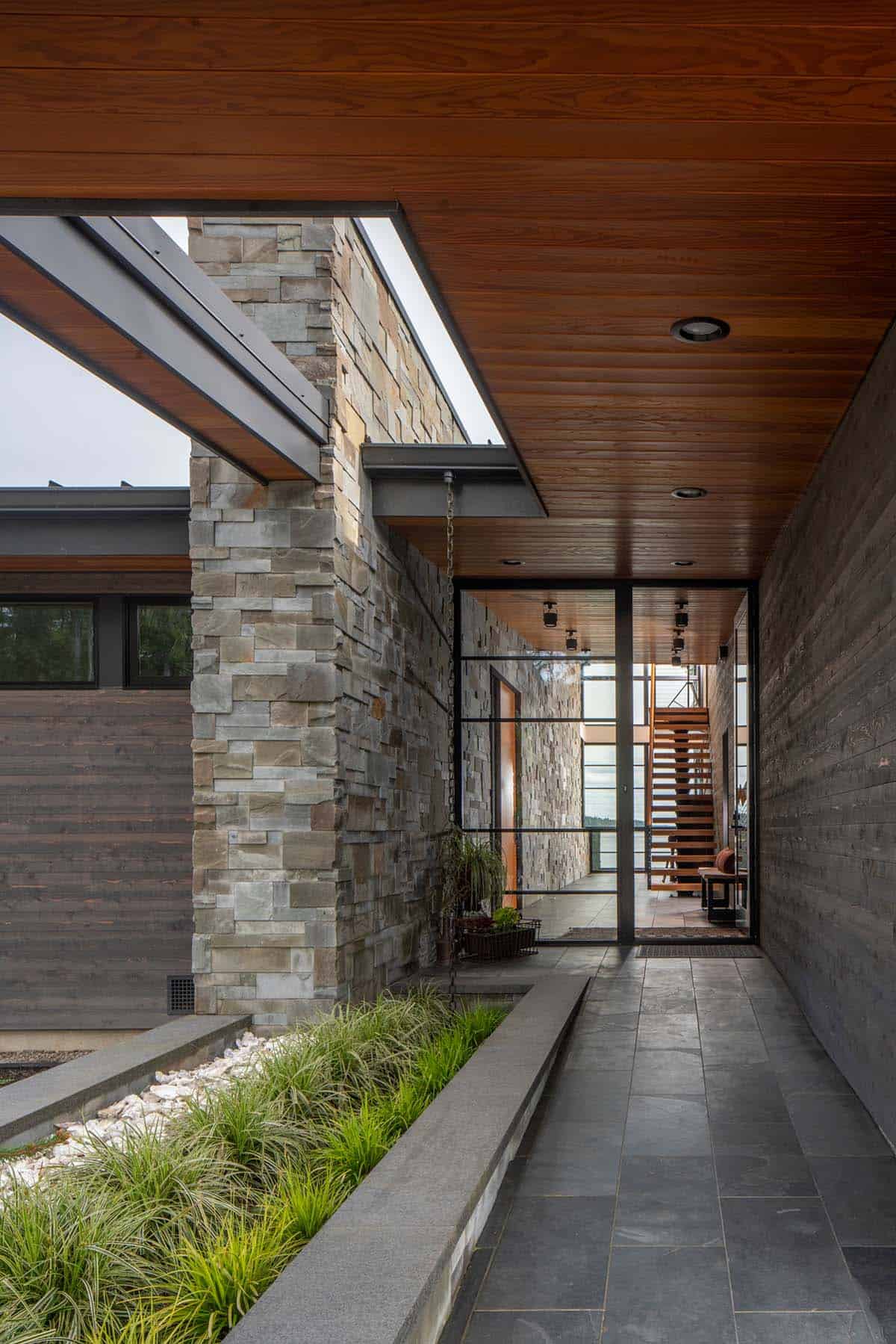 Covered walkway past a stone pillar leading to the glass entry