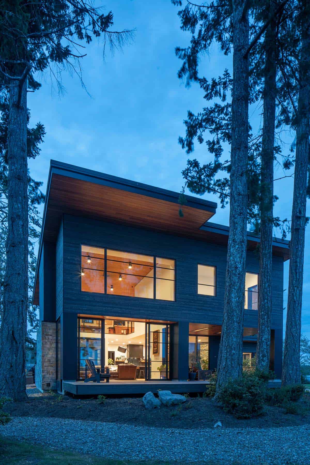 Illuminated two story home glows at dusk between tall pines