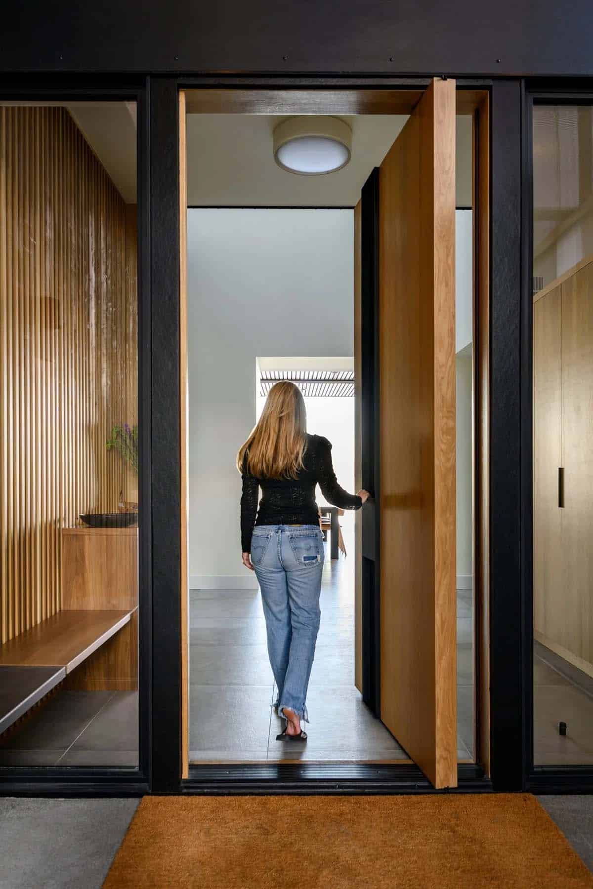 Woman viewed from behind walking through wood pivot door