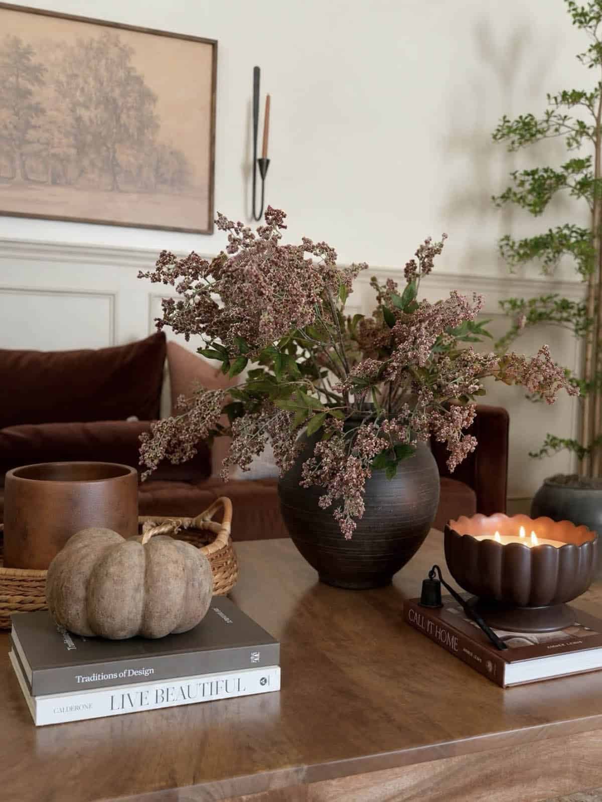 Dark vase with dusty pink berry stems beside pumpkin on stacked design books
