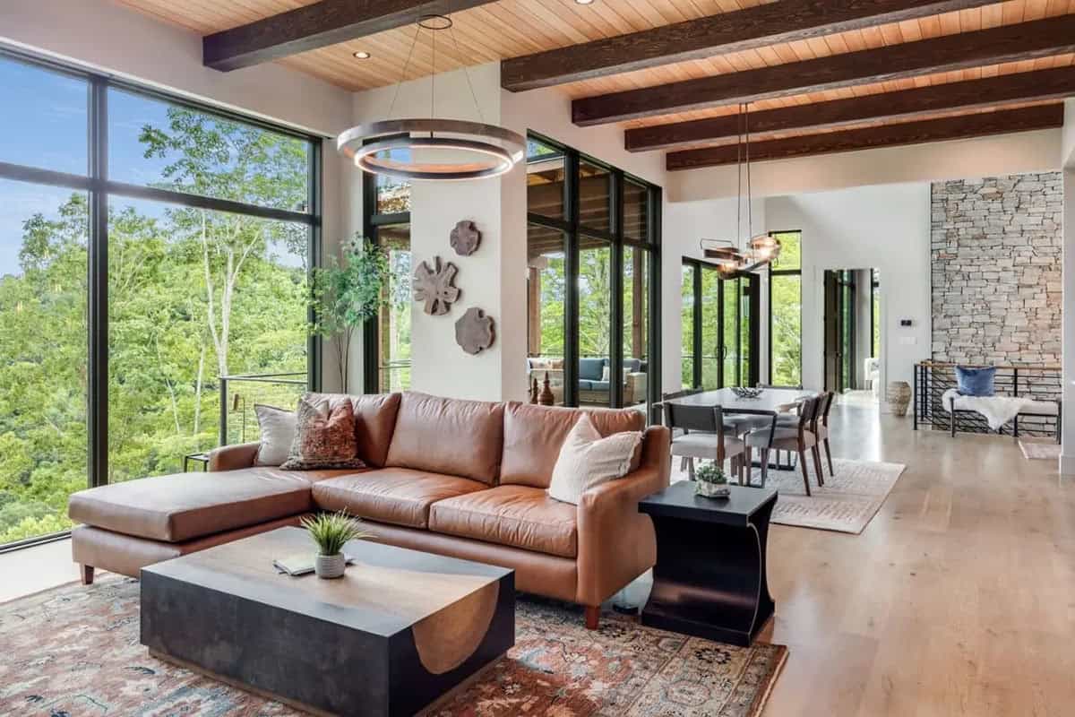Living room with leather sectional and floor to ceiling forest views