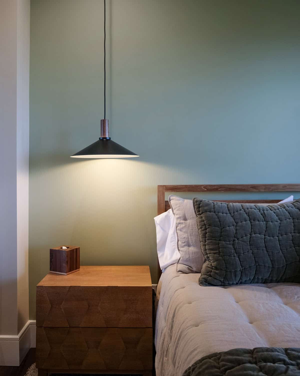 Bedroom pendant light above wood nightstand with sage walls