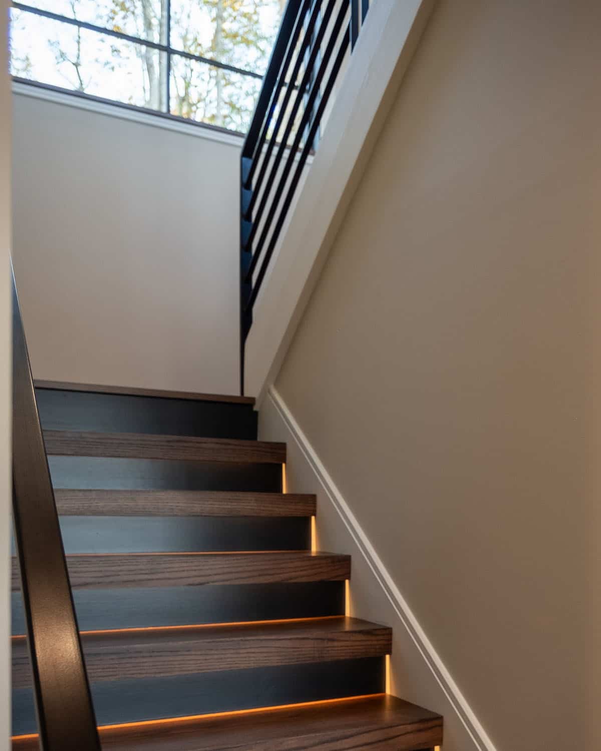 Wood staircase with integrated riser lighting and black railing
