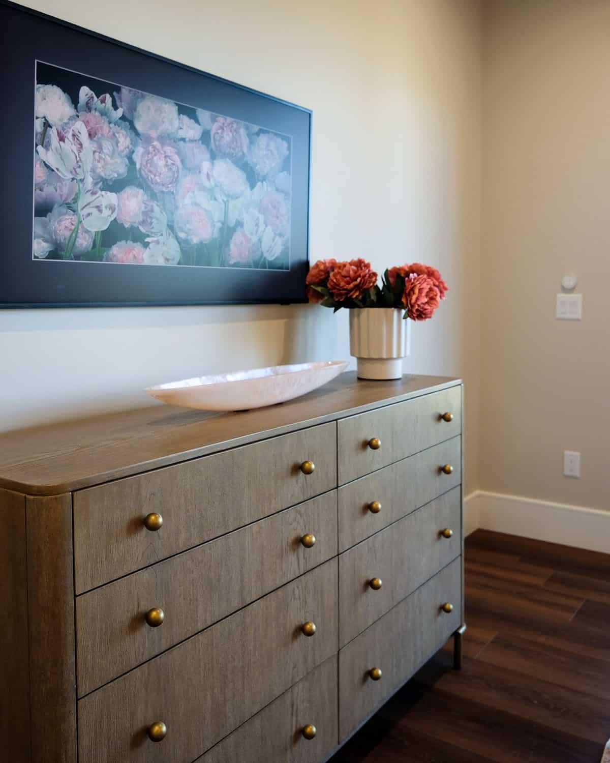 Bedroom dresser with wall-mounted TV and floral artwork