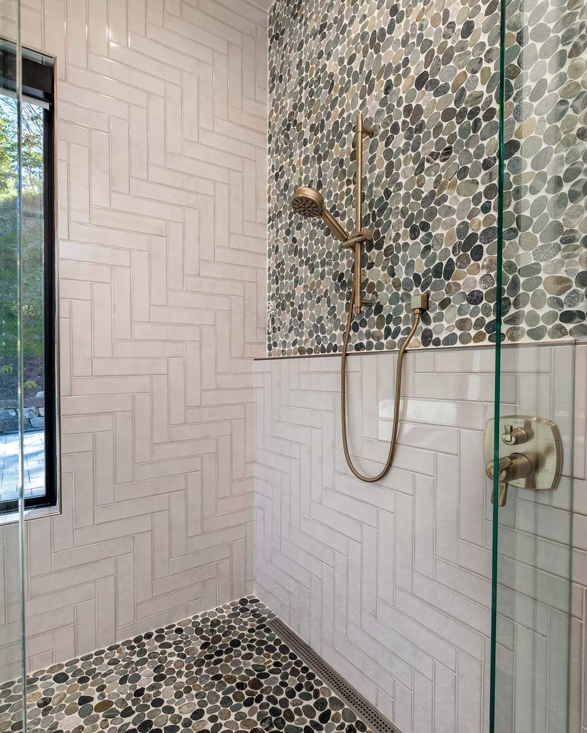 Herringbone tile shower with pebble accent wall and rain head
