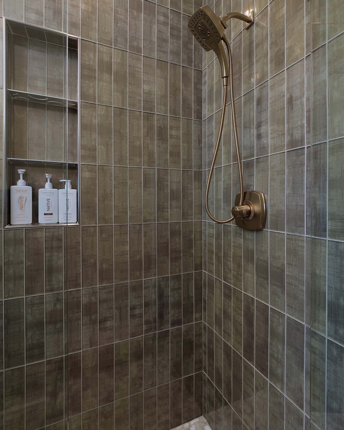 Vertical tile shower with brass fixtures and built-in niche