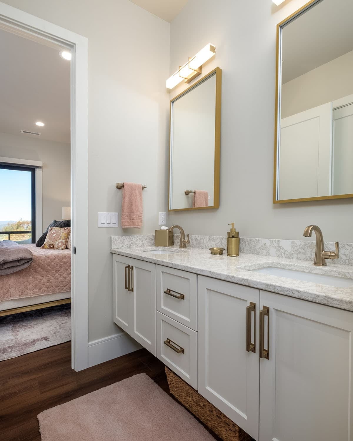 Bathroom double vanity with pink towel and bedroom view beyond