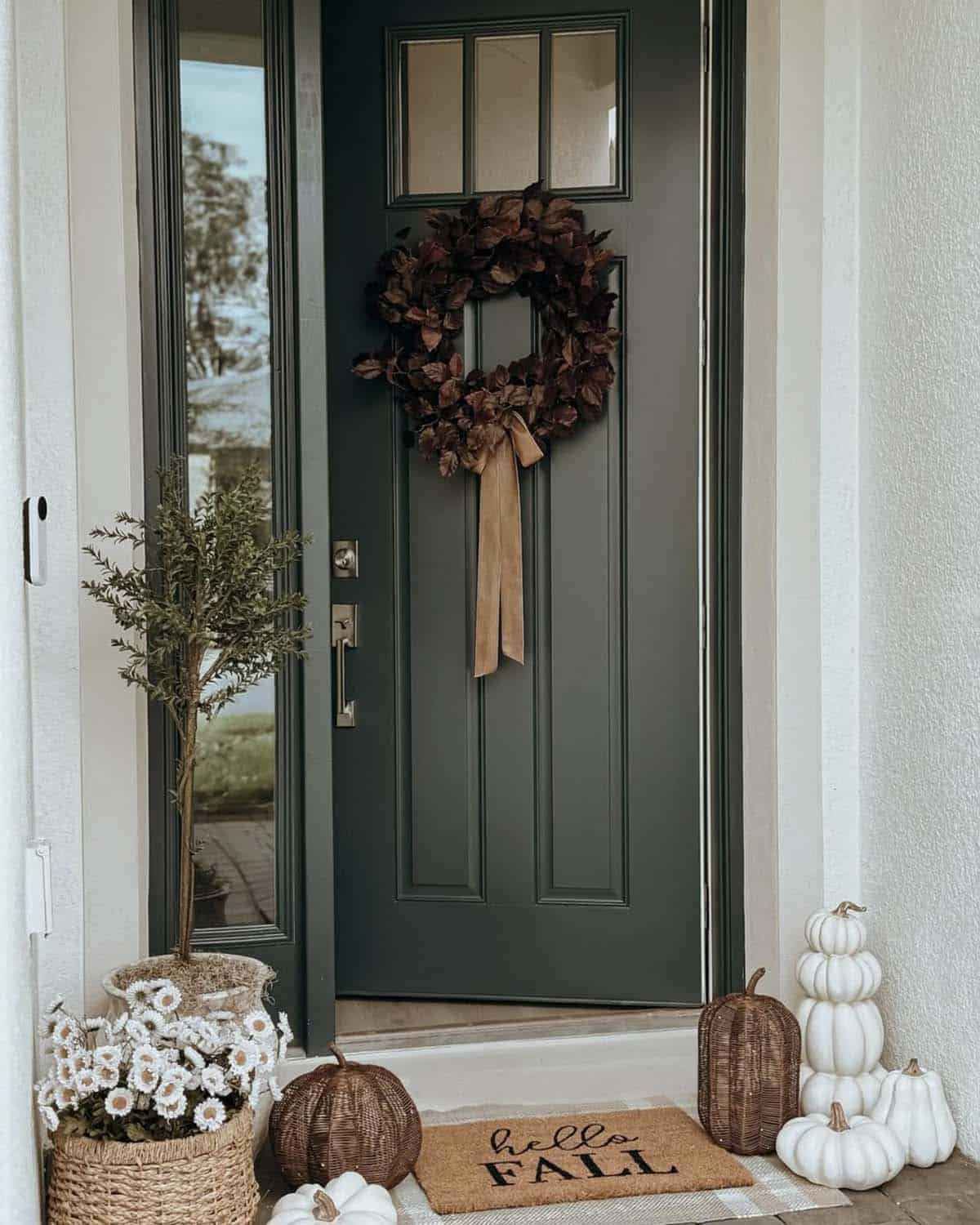 Green front door with wreath, woven pumpkins, white pumpkins, and olive tree