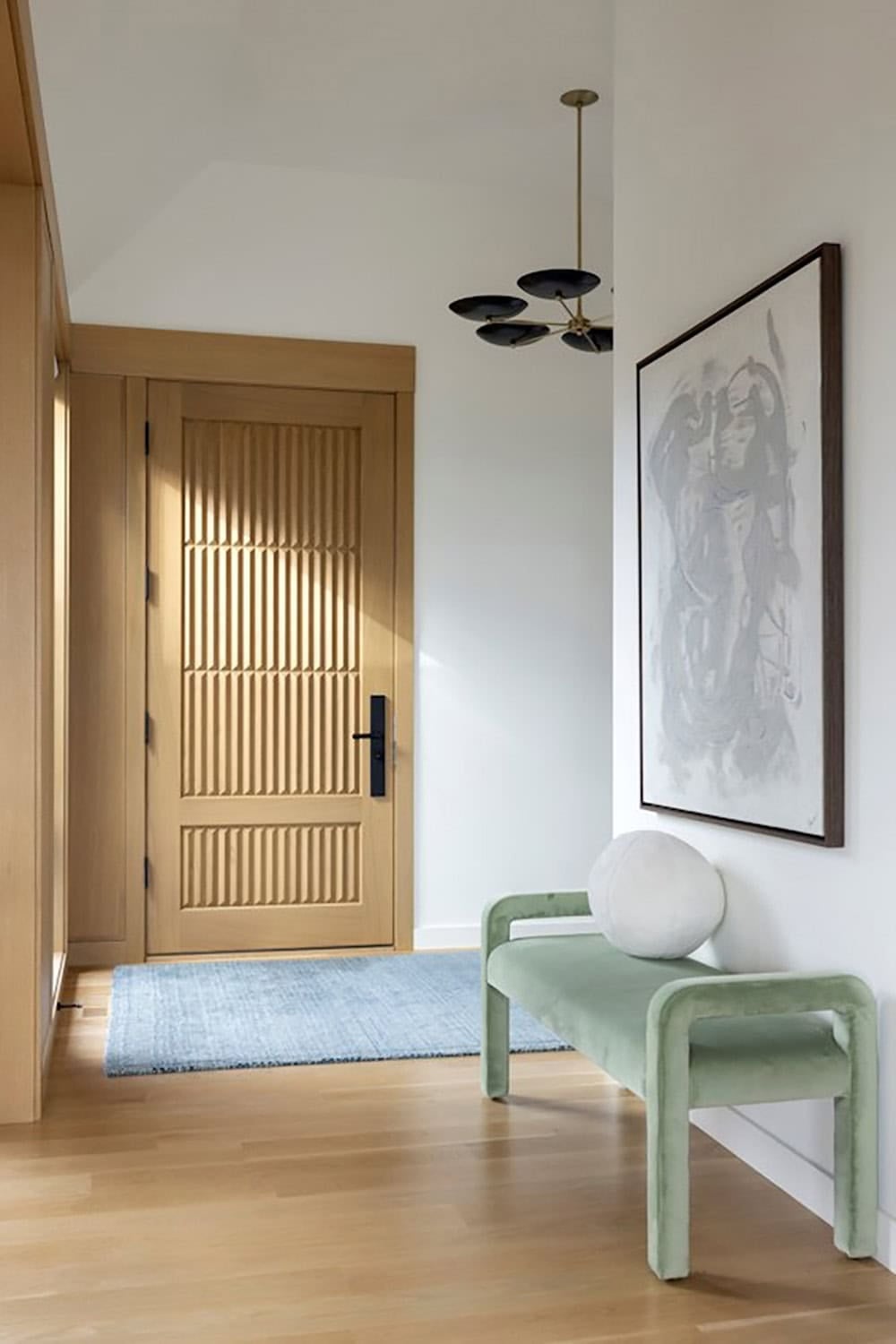 Entryway with slatted oak door, green bench, and abstract artwork