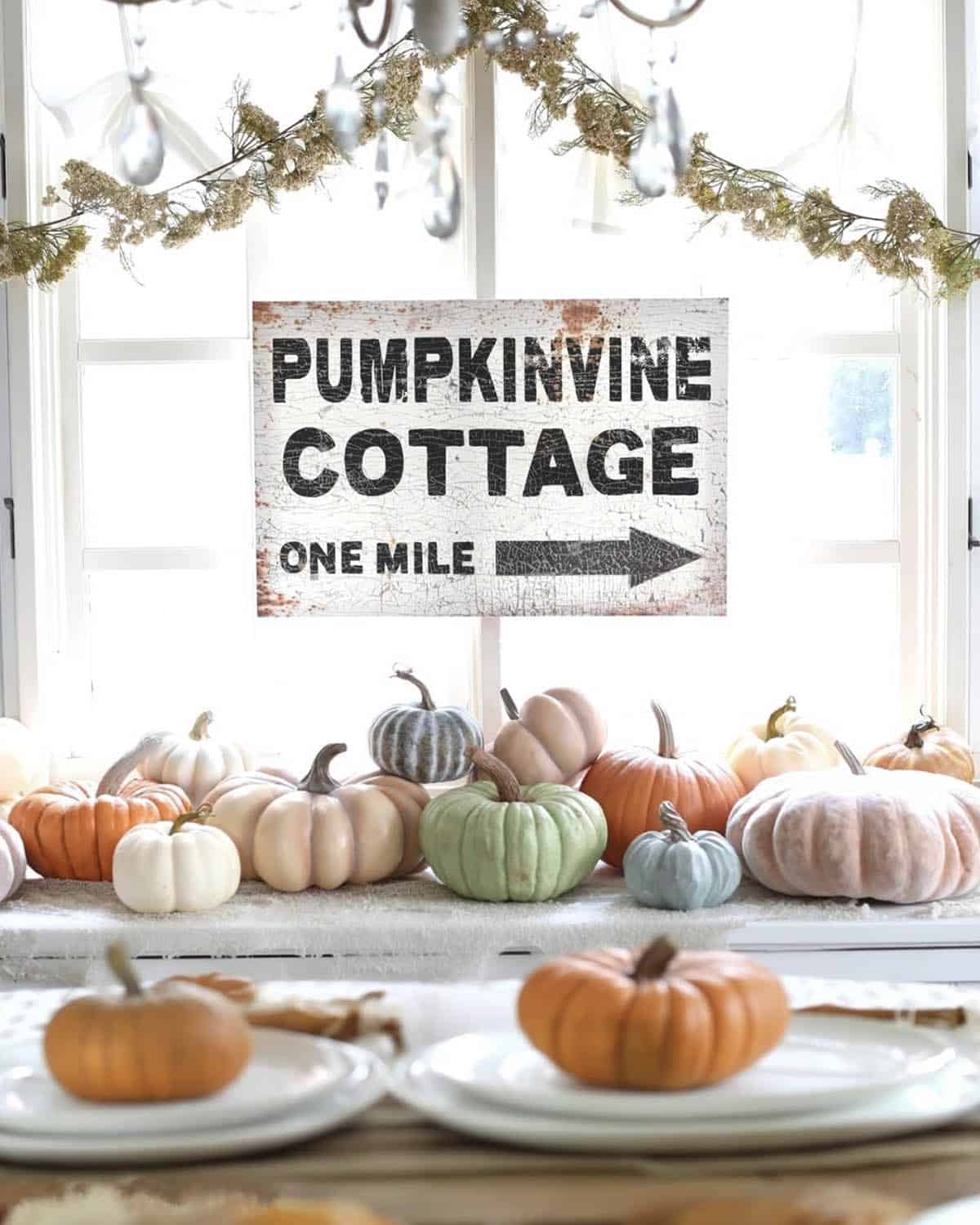 Row of pastel pink, sage, and gray pumpkins on window ledge with vintage sign
