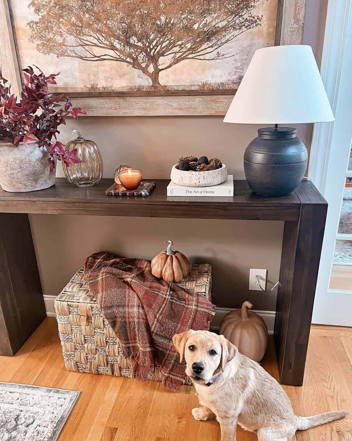 Woven basket with a plaid throw and pumpkins under a console table