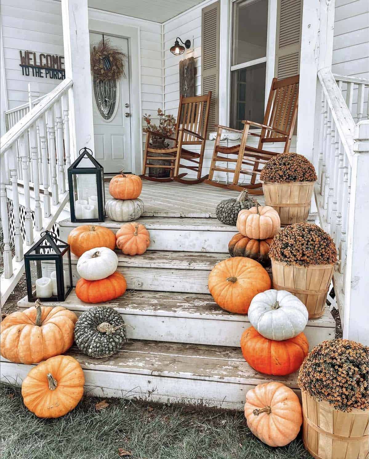 White porch steps layered with stacked pumpkins, gourds, lanterns, and mum baskets