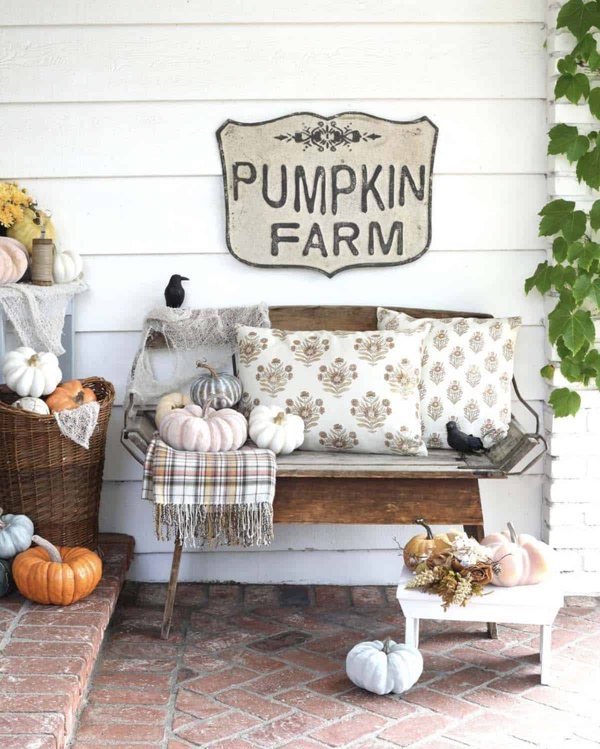 Wood bench with floral pillows, plaid throw, and pastel pumpkins under Pumpkin Farm sign