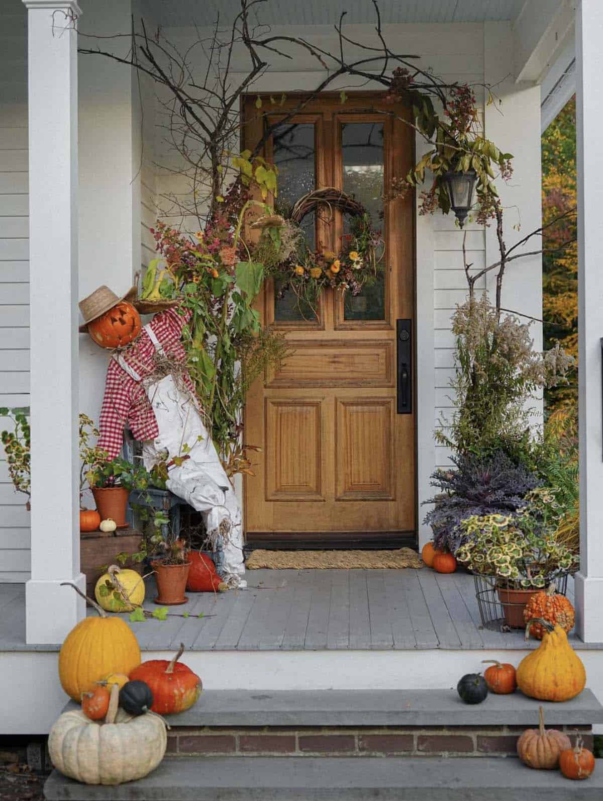 Fall porch with scarecrow, wood door, grapevine wreath, and pumpkins on steps