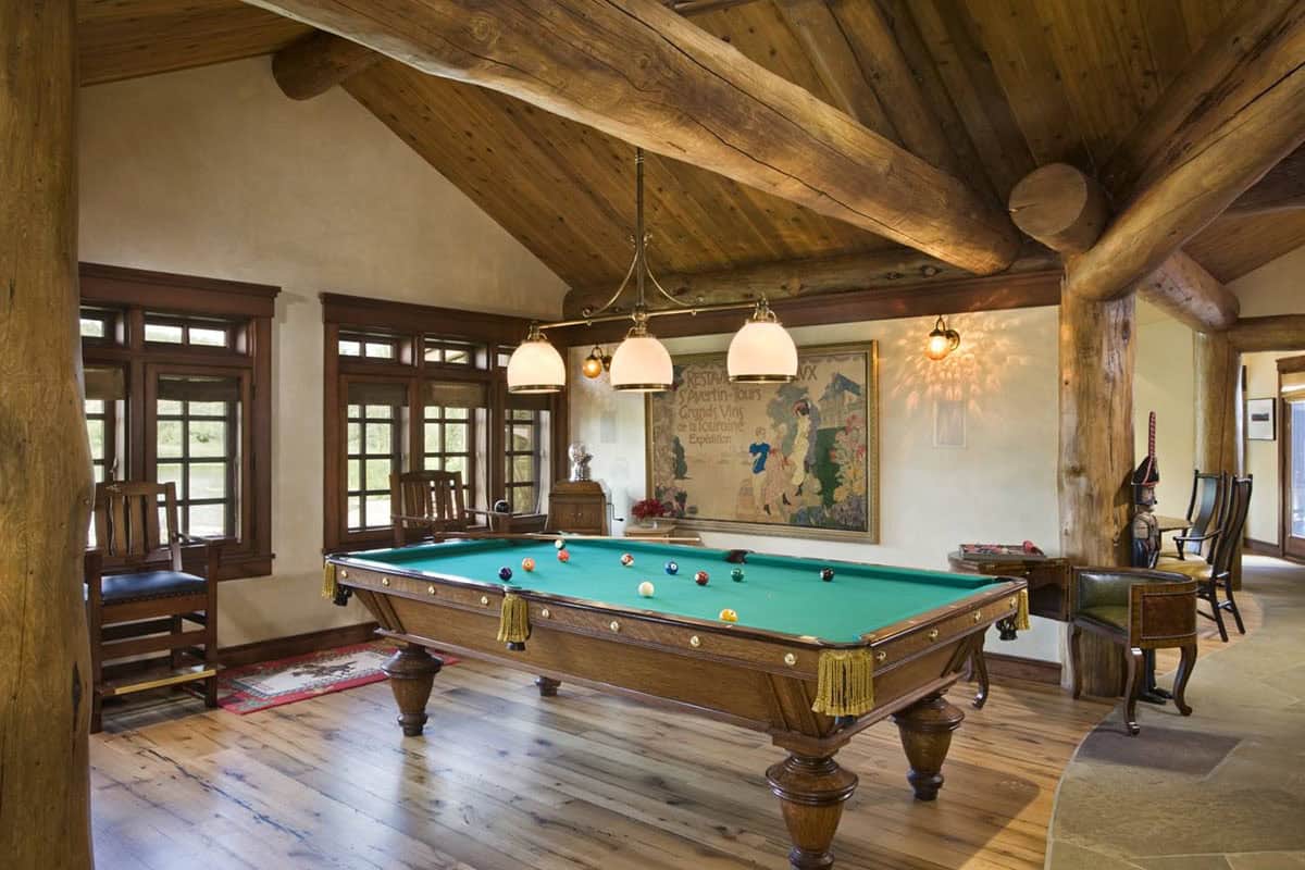 Game room with pool table under exposed log rafters