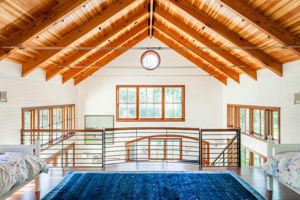 Loft sleeping area with exposed cedar rafters, steel cable ties, and a blue rug