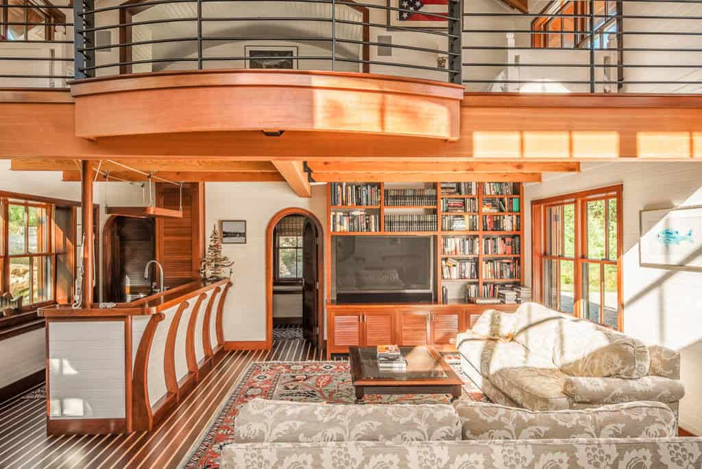 Open living area with nautical-style teak floors, built-in bookcase, and curved wood bar