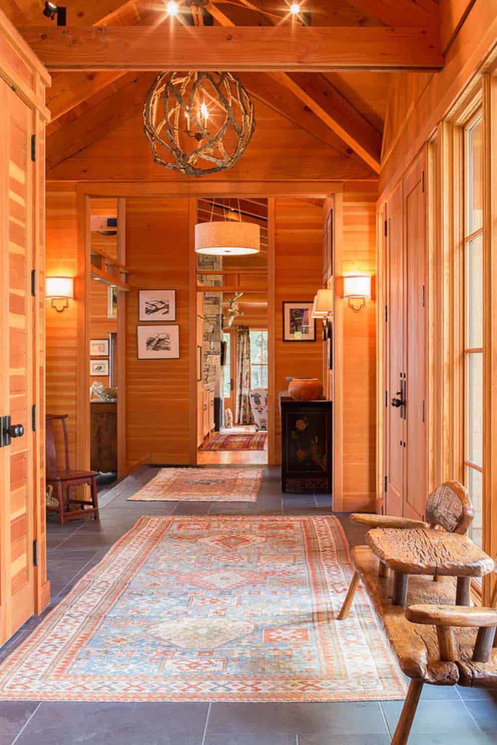 Entry hall with cedar-paneled walls, twig chandelier, and vintage blue runner