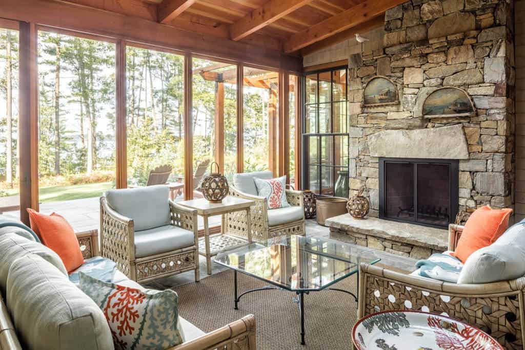 Screened porch with stone fireplace, wicker chairs, and orange coral pillows