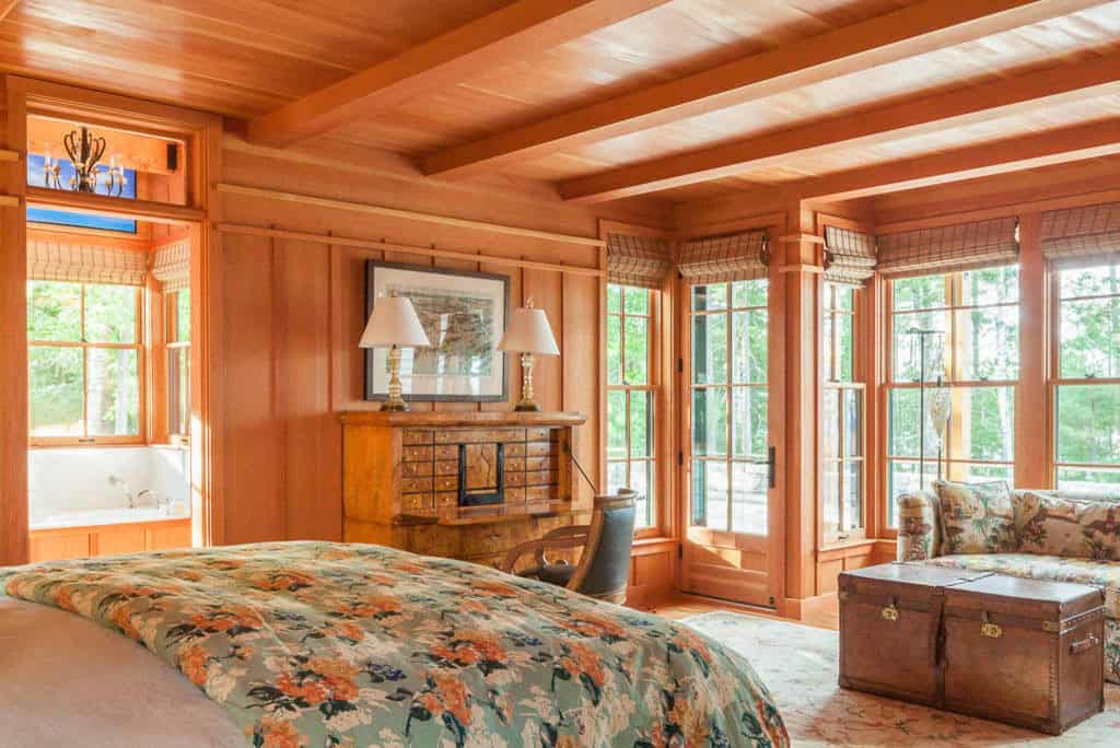 Primary bedroom with cedar paneling, antique desk, and wide wooded views